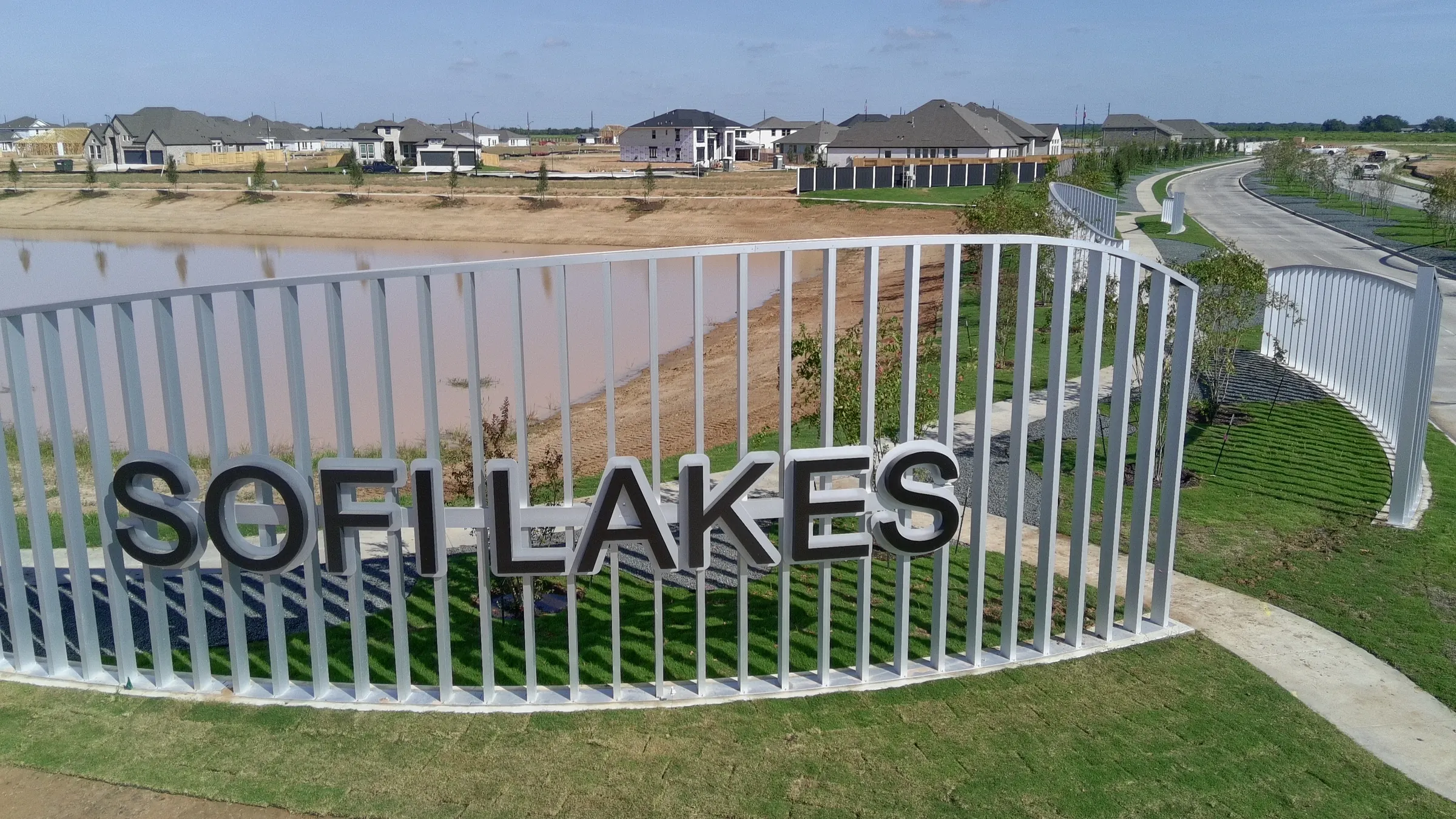 Sofi Lakes entrance monument sign in Katy, TX, with the lake and new homes behind it (aerial view)